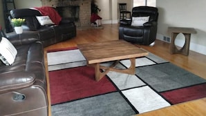 A living room with a fireplace, leather sofas, a wooden coffee table, and a patterned rug. - 21min from Buffalo Bills Stadium! Family-sized home with game room & firepit. (Springville)