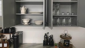 A kitchen with open cabinets displaying white dishes, a coffee maker, and a tea kettle. - 21min from Buffalo Bills Stadium! Family-sized home with game room & firepit. (Springville)