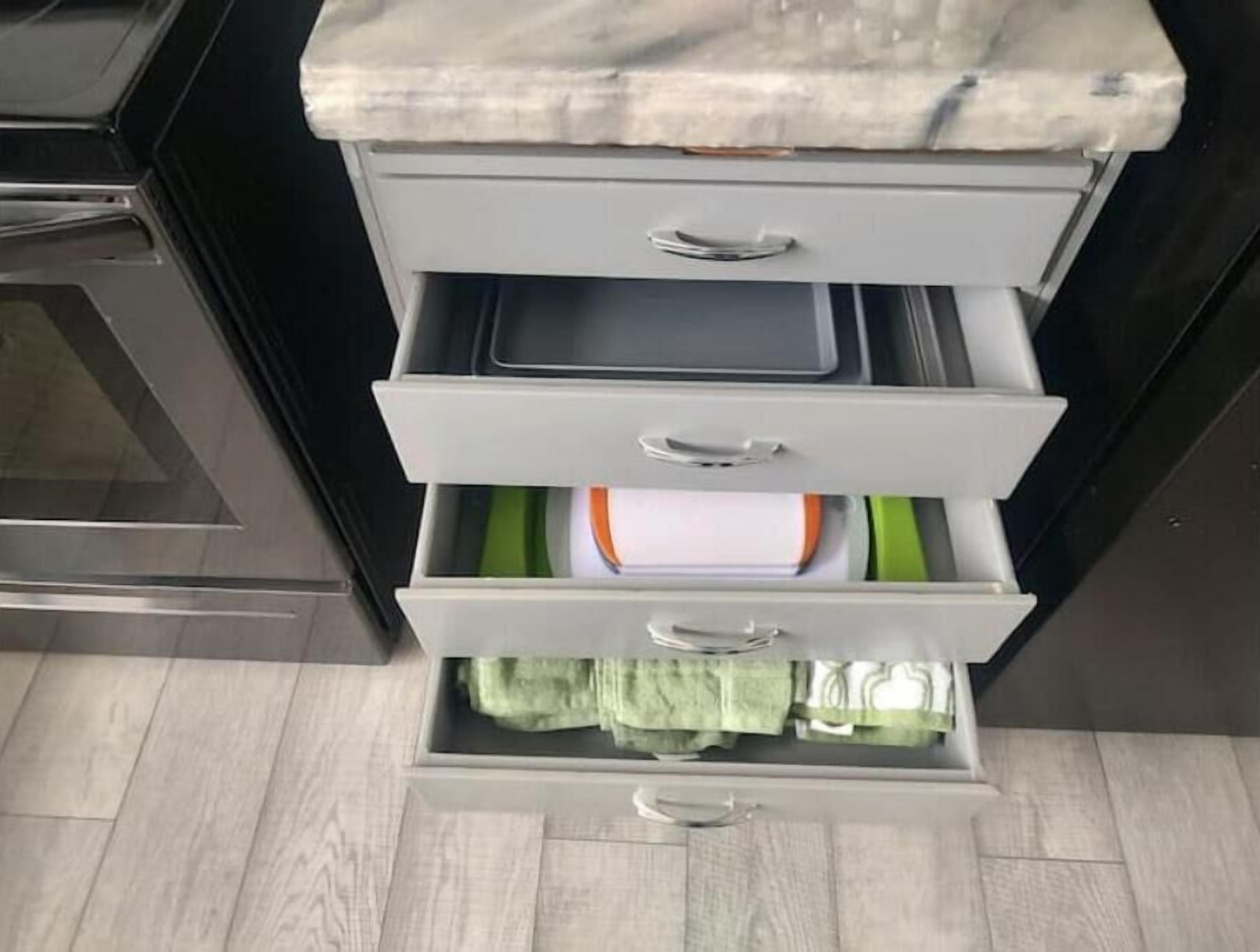 A kitchen with a countertop, a stove, and a drawer with green towels.