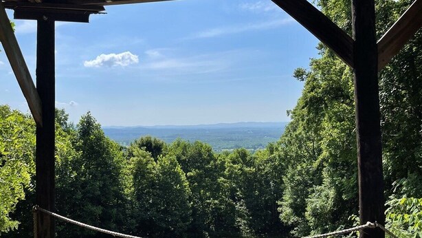 A covered outdoor area with a rope barrier, wooden beams, and a view of a forested landscape. - Mountain house in Fancy Gap with beautiful view and hot tub on deck (Fancy Gap)