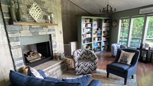 A cozy living room with a stone fireplace, a ceiling fan, a bookshelf, and a comfortable seating area. - Mountain house in Fancy Gap with beautiful view and hot tub on deck (Fancy Gap)