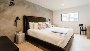 A modern bedroom with a large bed, bedside lamps, a small table, and a window.