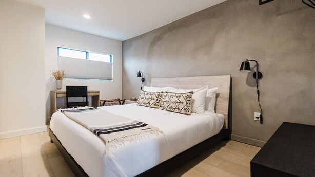 A modern bedroom with a large bed, bedside lamps, a desk, and a window with blinds.