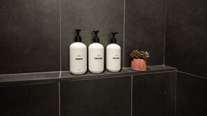 Three bottles of shampoo, conditioner, and body wash on a dark tiled shelf.