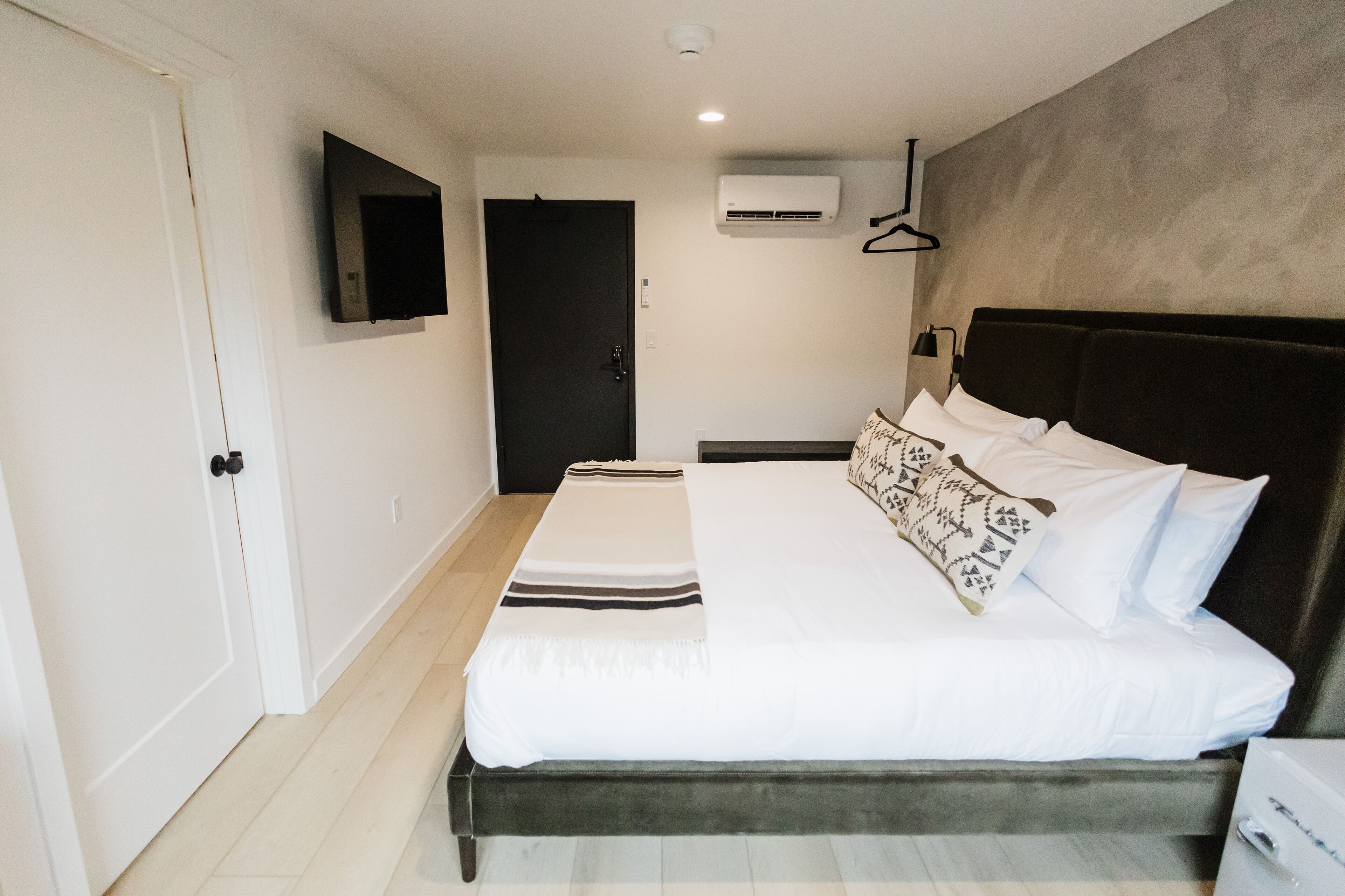 Un dormitorio con una cama, un televisor montado en la pared, un equipo de aire acondicionado y una puerta.