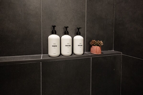 Three bottles of shampoo, conditioner, and body wash on a dark tiled shelf.