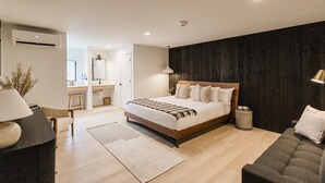 A modern bedroom with a wooden bed, a sofa, a desk, and a lamp.