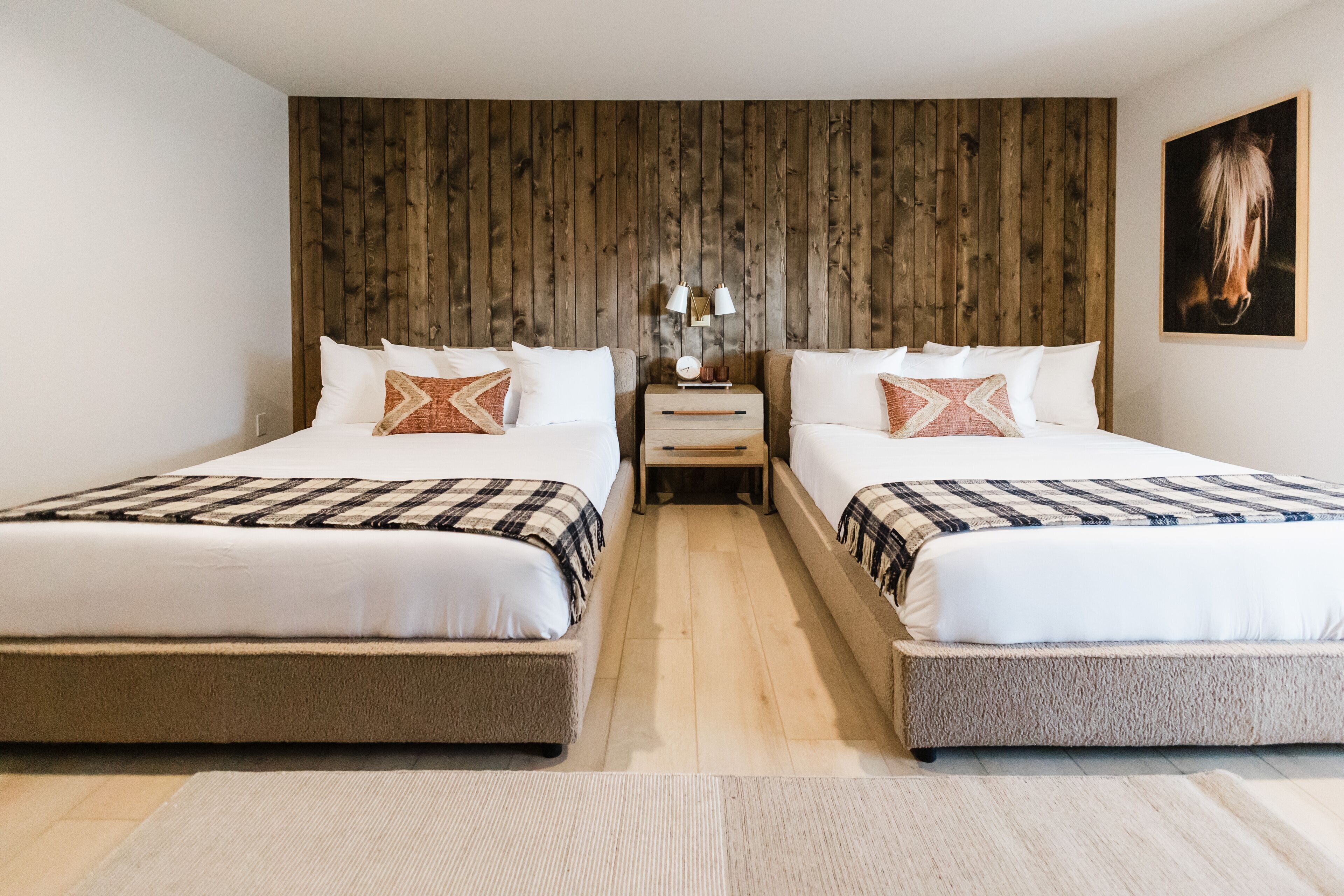 Habitación doble con dos camas, cabecero de madera, mesita de noche con lámparas y un cuadro enmarcado en la pared.