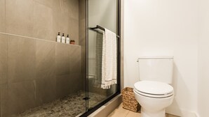 Een moderne badkamer met een douchecabine van glas, een wit toilet en een plank met toiletartikelen.