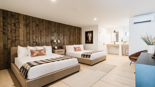 Een moderne hotelkamer met twee bedden, een wand van hout, een bureau en een badkamer op de achtergrond.