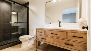 Une salle de bain moderne avec une douche à parois de verre, des toilettes blanches et un meuble-lavabo en bois avec un miroir.
