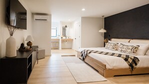 A modern bedroom with a large bed, bedside tables, a flat-screen TV, and an air conditioning unit. - Wonderstone Hotel - Single King ADA Guest Room (Columbia Falls)