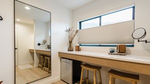 A modern kitchen with a large mirror, wooden stools, a built-in refrigerator, and a window with blinds. - Wonderstone Hotel - Single King ADA Guest Room (Columbia Falls)