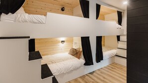 A bunk bed room with wooden flooring, white bedding, and black curtains. - Wonderstone Bunkhouse (Individual Bed) (Columbia Falls)