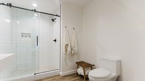 Une salle de bain moderne avec une douche à parois de verre, des toilettes et un petit tabouret en bois.