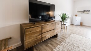 Un salon moderne avec un grand téléviseur à écran plat fixé sur un meuble en bois, une plante en pot et un meuble blanc avec un plateau en bois.