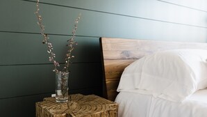 A bed with white bedding, a wooden headboard, and a nightstand with a vase of branches. - Wonderstone Single King Guest Room (Columbia Falls)