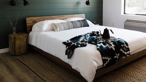 A neatly made bed with a wooden headboard, a patterned throw blanket, and a bedside table with a lamp. - Wonderstone Single King Guest Room (Columbia Falls)