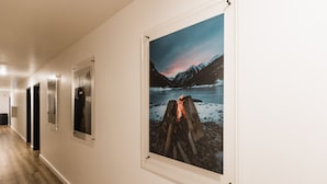 A hallway with framed pictures on the wall, a wooden floor, and a door at the end. - Wonderstone Single Queen ADA Guest Room (Columbia Falls)