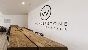 A long wooden table in a modern room with a white wall and a logo that reads "WONDERSTONE GLACIER". - Wonderstone Single Queen ADA Guest Room (Columbia Falls)