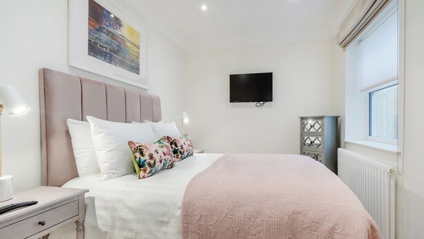 Ein ordentlich eingerichtetes Schlafzimmer mit Bett, Nachttisch, Lampe und einem an der Wand befestigten Fernseher.
