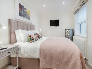 A neatly arranged bedroom with a bed, bedside table, lamp, and a TV mounted on the wall.
