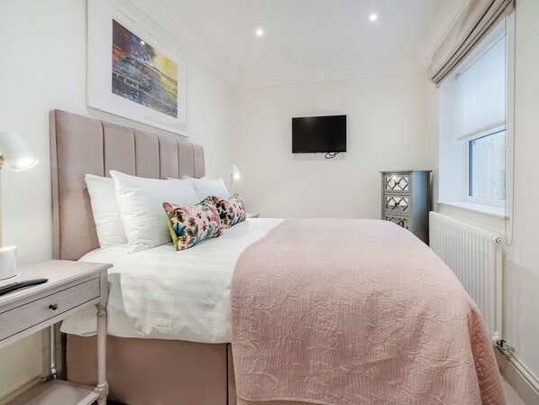 A neatly arranged bedroom with a bed, bedside table, lamp, and a TV mounted on the wall.