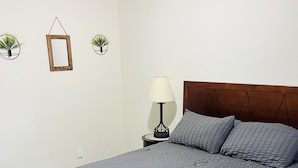 A neatly made bed with a dark quilt, a wooden headboard, and a bedside table with a lamp.