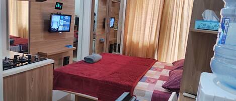 Una habitación de hotel compacta con cama, una kitchenette pequeña, televisión y dispensador de agua.