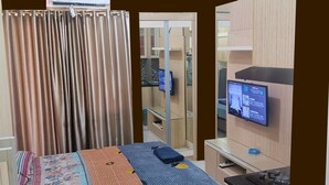 Un dormitorio con cama, televisión, escritorio y baño con espejo e inodoro.