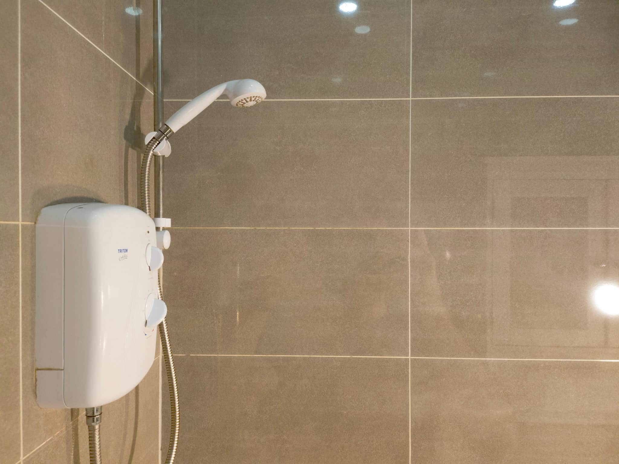 A shower with a handheld showerhead and a wall-mounted control panel.