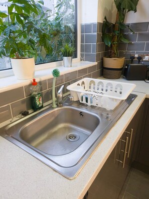 A kitchen with a stainless steel sink, a window with plants, and a tiled backsplash.