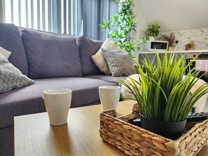 Un salon moderne avec un canapé, deux tasses blanches, un plateau en osier et une plante verte.