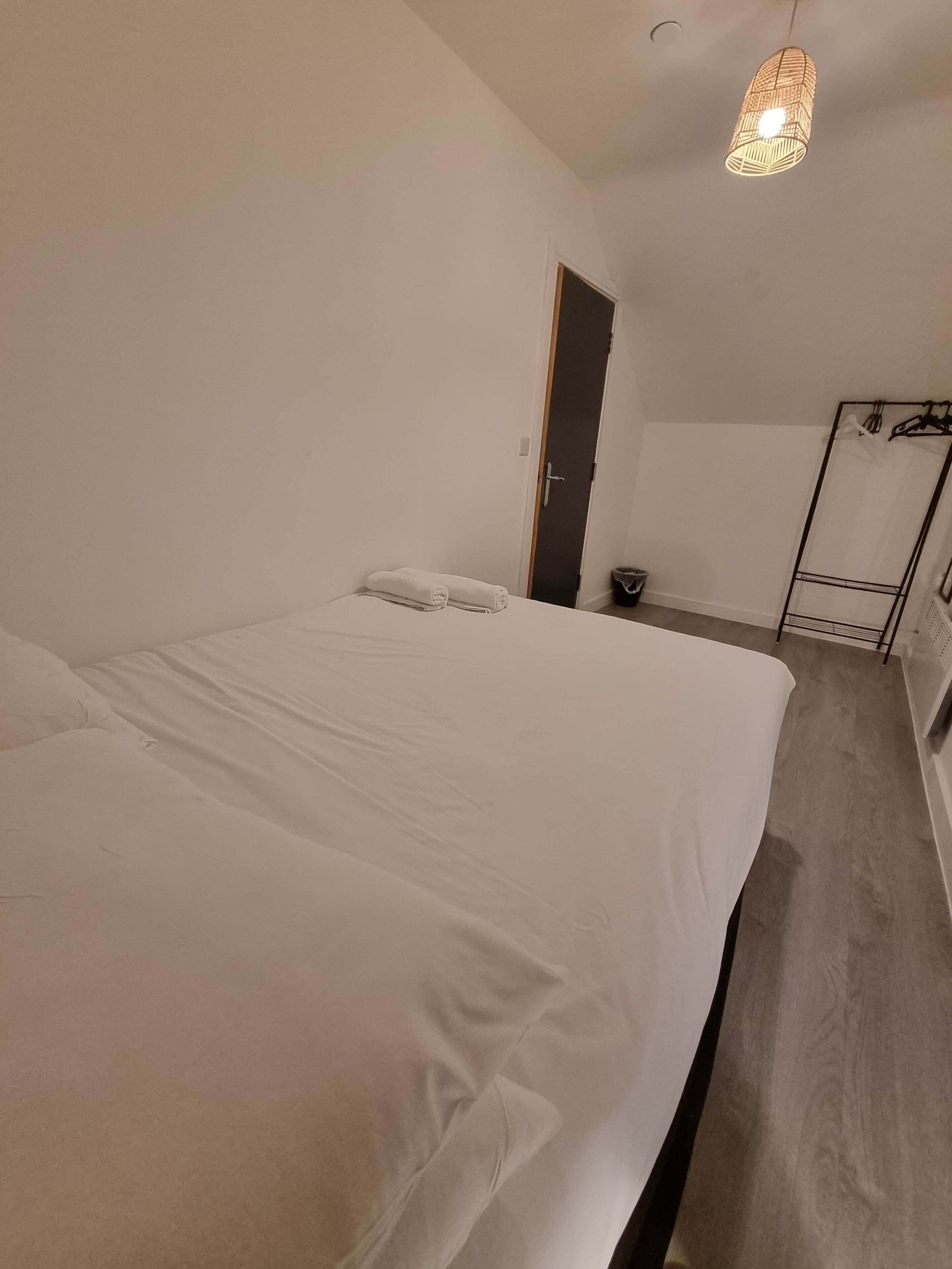 A bedroom with a large bed, a wardrobe, a hanging light fixture, and a door.
