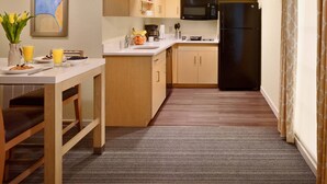 Una cocina compacta con armarios de madera, un refrigerador negro, un microondas y un comedor con mesa y sillas.