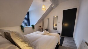 Un dormitorio moderno con una cama grande, una mesita de noche pequeña, un espejo y una ventana con persianas.