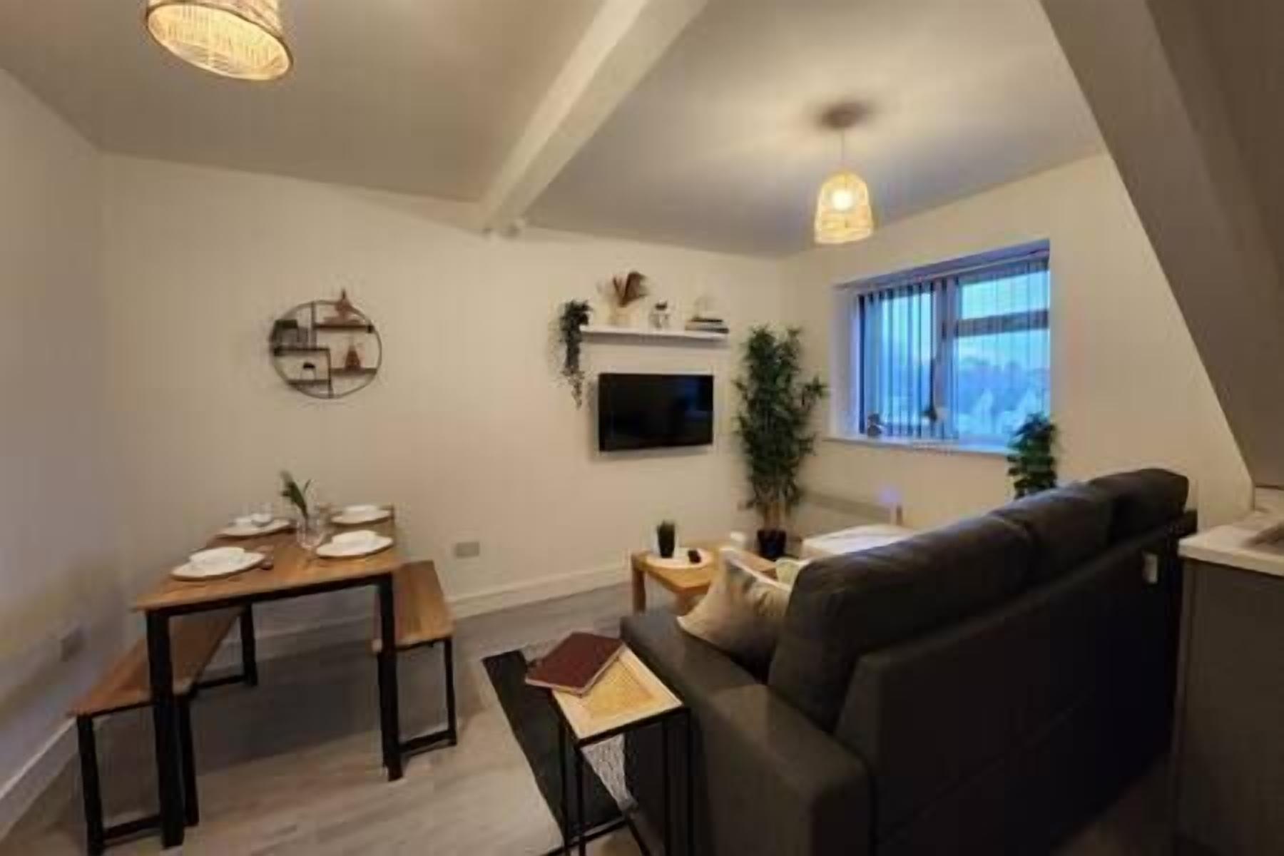 A modern living room with a sofa, a dining table, and a TV mounted on the wall.