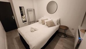A modern bedroom with a bed, pillows, a round mirror, and a small round table. - ApartHotel - Flat 6 (1 bed) (Cardiff)