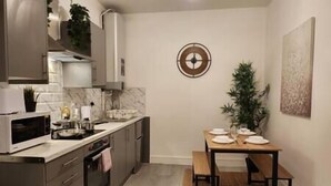 A compact kitchen with modern appliances, a dining table set for four, and a decorative wall clock. - ApartHotel - Flat 6 (1 bed) (Cardiff)