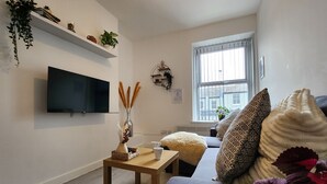 Un salon moderne avec un téléviseur à écran plat, une table basse en bois et un canapé agrémenté de coussins à motifs.