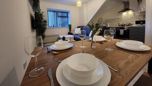 A dining area with a wooden table set for four, a kitchen in the background, and a living room with a blue sofa.