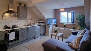 A modern kitchen with a built-in oven, microwave, and a large window. There is a sofa and a small table in the living area.