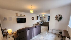 A modern living room with a large sectional sofa, a flat-screen TV, and a dining area with a small table and chairs. - ApartHotel - Flat 8 (2 bed) (Cardiff)
