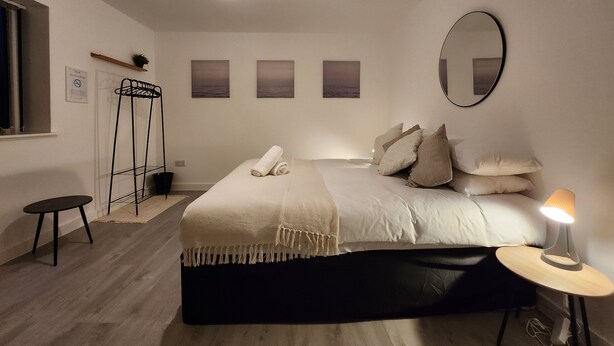 A bedroom with a bed, a bedside lamp, a mirror, and artwork on the wall. - ApartHotel - Flat 8 (2 bed) (Cardiff)