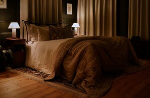 Ein schummrig beleuchtetes Hotelzimmer mit Bett, zwei Nachttischlampen, einem Nachttisch und einem gemusterten Teppich.