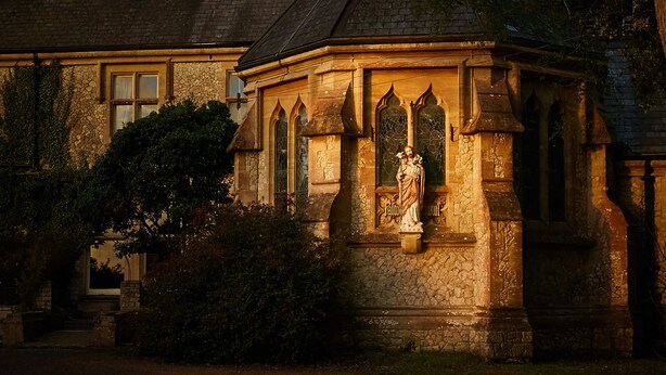 Un edificio de piedra con una estatua en su fachada, rodeado de árboles.