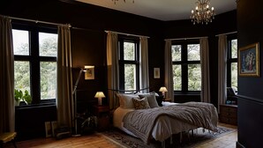 Un dormitorio con una cama grande, varias ventanas, una araña y una mesita de noche con lámpara.