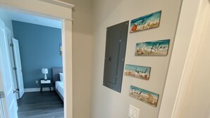 Een gang met een houten vloer, een deur aan de rechterkant en een wand met ingelijste kunstwerken.