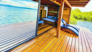 A wooden deck with a bed and lounge chairs overlooking a body of water.