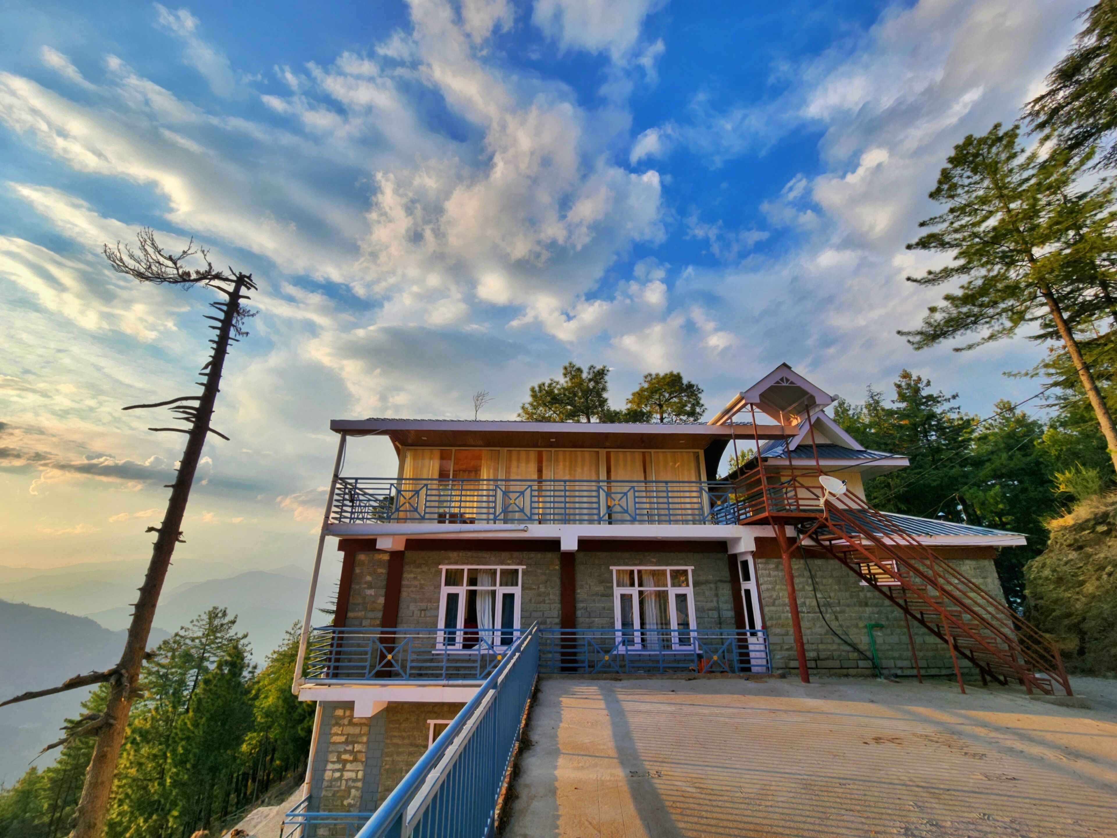 A two-story building with a balcony, a staircase, and a view of the mountains.